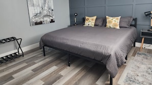 A modern bedroom with a grey bed, a black metal frame, a grey headboard, and a black nightstand with a lamp. - Cozy getaway mins from Michigan Tech, Ski & Snowmobile trails & Lake Superior (Hancock)