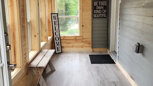 A wooden interior with a bench, a welcome sign, and a view of greenery outside. - Cozy getaway mins from Michigan Tech, Ski & Snowmobile trails & Lake Superior (Hancock)