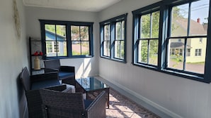 A sunroom with a glass table, wicker chairs, and large windows offering a view of the neighborhood. - Cozy getaway mins from Michigan Tech, Ski & Snowmobile trails & Lake Superior (Hancock)