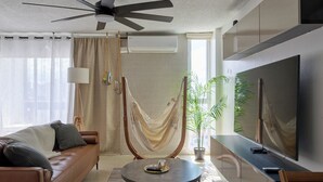 Un salon moderne avec un canapé en cuir marron, une table basse ronde, un hamac, un grand téléviseur à écran plat et une plante en pot.
