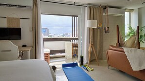 Une chambre d’hôtel équipée d’un lit, d’un tapis de sol pour les exercices, d’un tapis de yoga et offrant une vue sur la ville grâce à de grandes fenêtres.