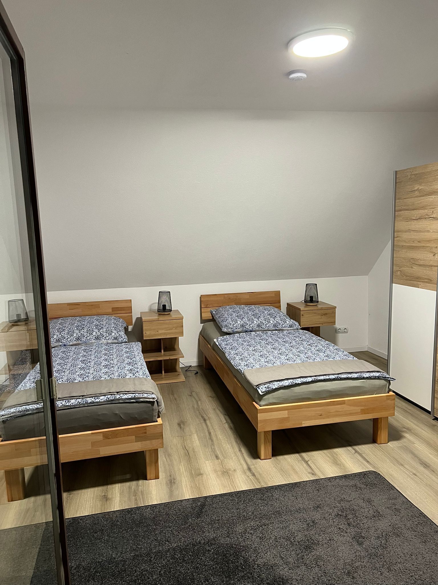A modern bedroom with two wooden beds, a glass partition, and a wooden wardrobe.