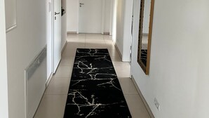 A hallway with white walls, a black marble rug, and a large mirror on the right.