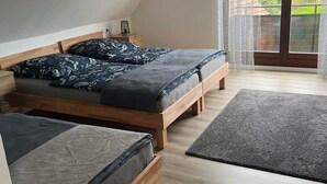A bedroom with two wooden beds, a small bedside table, a nightstand, and a view of the outside through a large window.