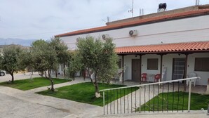 Un edificio residenziale con tetto in tegole, un portico coperto e un piccolo giardino con alberi e prato.