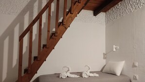 Una camera da letto con una scala in legno, un letto con copriletto trapuntato, due asciugamani bianchi, un cuscino bianco, un comodino e un punto luce a parete.