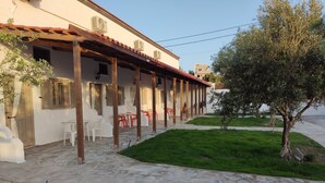 Un'area salotto esterna riparata con pavimento in pietra, sedie di plastica bianche e rosse, e un albero sullo sfondo.