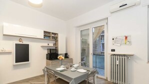 A modern kitchen with white cabinets, a dining table set with plates, and a view through a glass door to a balcony.