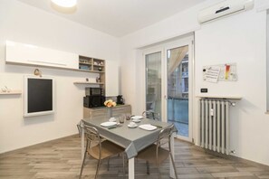 A modern kitchen with white cabinets, a dining table set with plates, and a view through a glass door to a balcony.
