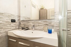 Un bagno con un lavandino bianco, uno specchio, un box doccia in vetro e un armadietto in legno.