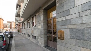 A multi-story building with a stone facade, a ground-floor entrance with a mailbox, and parked cars along the street.