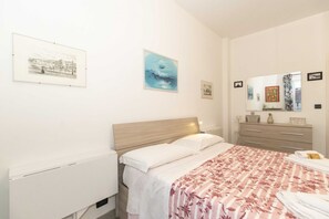 Ein Schlafzimmer mit Bett, Schminktisch, Spiegel und Wandbildern.