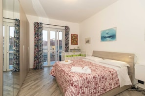Ein Schlafzimmer mit Bett, Vorhängen am Fenster, einer Tür und einem Bild an der Wand.