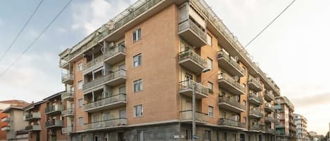 Un edificio residencial de varios pisos con balcones, coches estacionados y un cielo despejado.