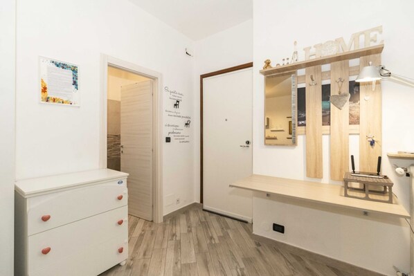A room with a white dresser, a mirror with a 'HOME' sign, and a wooden shelf with a lamp.