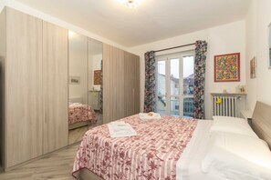 Quarto com cama, guarda-roupa, radiador e janela com cortinas.