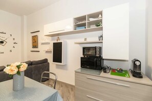 Uma cozinha moderna com micro-ondas, torradeira e máquina de café no balcão, um sofá cinzento e uma mesa de jantar com um vaso de flores.