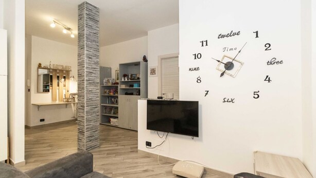 A modern living room with a flat-screen TV mounted on the wall, a stone pillar, and a bookshelf.