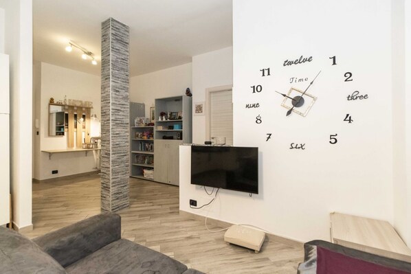 A modern living room with a flat-screen TV mounted on the wall, a stone pillar, and a bookshelf.