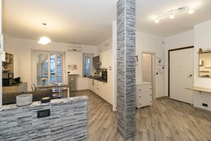 Uma cozinha moderna com uma ilha central, uma sala de jantar com mesa e cadeiras, e uma sala de estar com sofá e televisão.