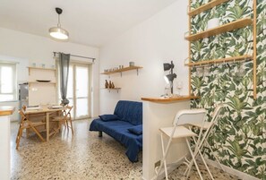 Ein kompakter Wohnraum mit Essbereich, einer Couch, einem kleinen Tisch und einer Wand mit Blätermotiv.