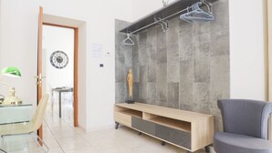 A modern living room with a wooden entertainment unit, a grey tiled wall, a green desk lamp, and a grey chair. - GuestHost - Veiled Christ Bilo Apartment (Napoli)