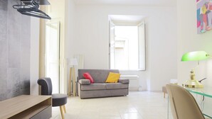 A modern living room with a sofa, a glass coffee table, a wooden side table, a lamp, and a chair. - GuestHost - Veiled Christ Bilo Apartment (Napoli)