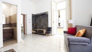 A modern living room with a grey sofa, a wooden cabinet, and a black wall-mounted shelf. - GuestHost - Veiled Christ Bilo Apartment (Napoli)