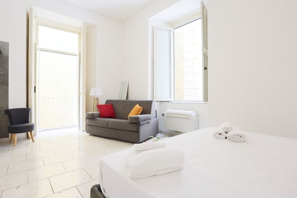 A hotel room with a bed, a sofa, a chair, and a radiator.