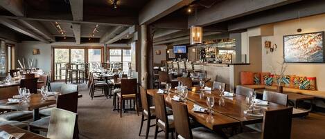 Un restaurante con varias mesas, sillas y una zona de bar.