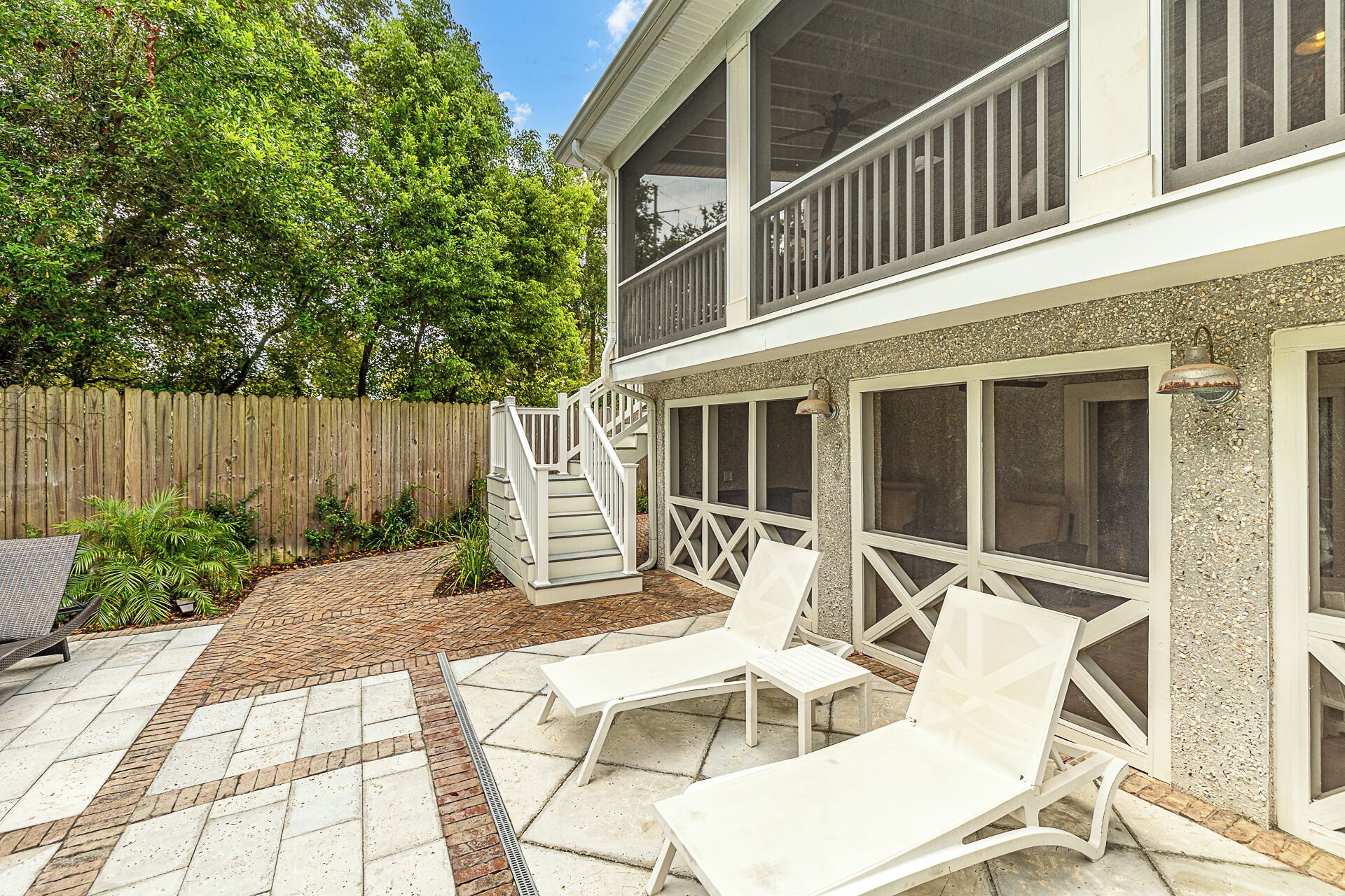 A two-story house with a balcony, a covered patio with lounge chairs, and a wooden fence.