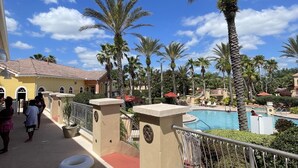 Ein Poolbereich eines Resorts mit Palmen, einer gefliesten Terrasse und einem Gebäude mit Rundbogenfenstern.
