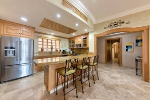 Uma cozinha espaçosa com uma ilha grande, eletrodomésticos de aço inoxidável e um espaço bar com banquetas.