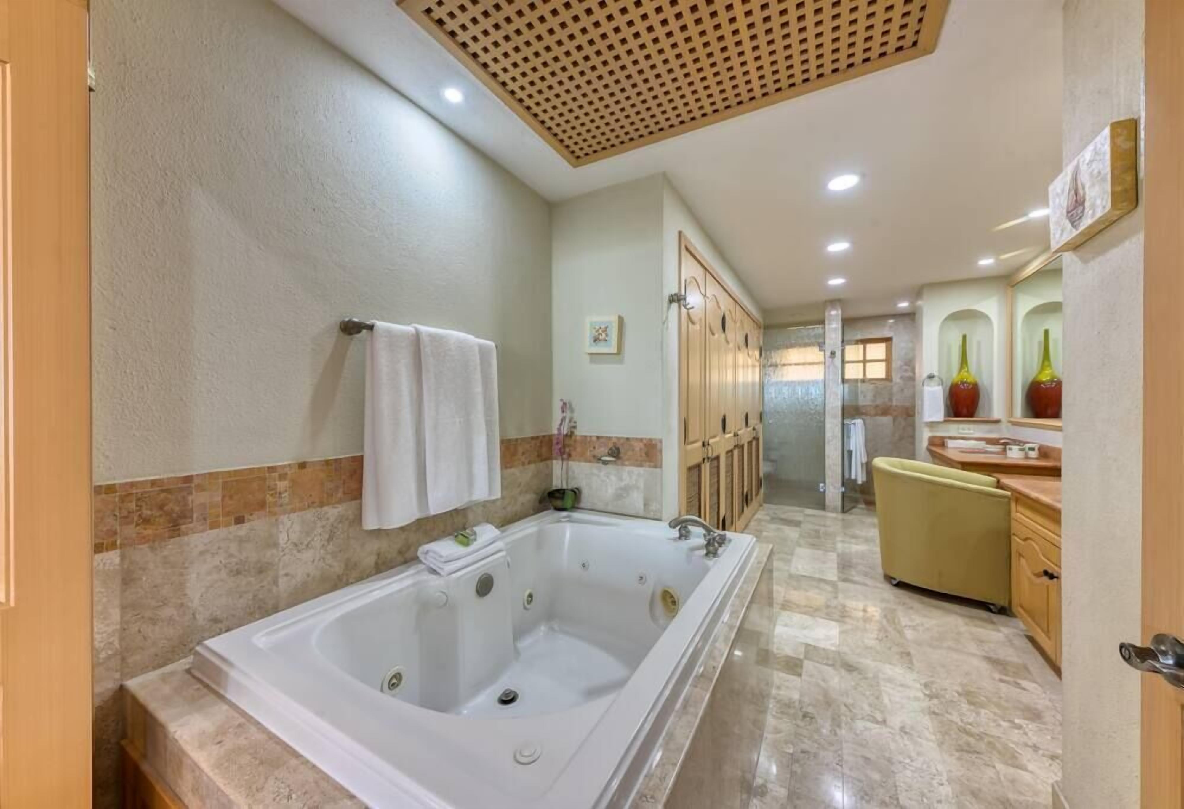 A spacious bathroom with a large bathtub, a wooden door, and a yellow chair.