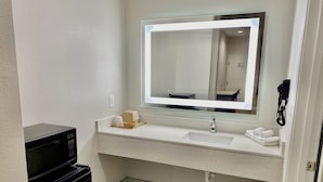 A hotel bathroom with a white sink, a mirror with lights, a black telephone, and a trash can. - Bluestar Inn (Houston)