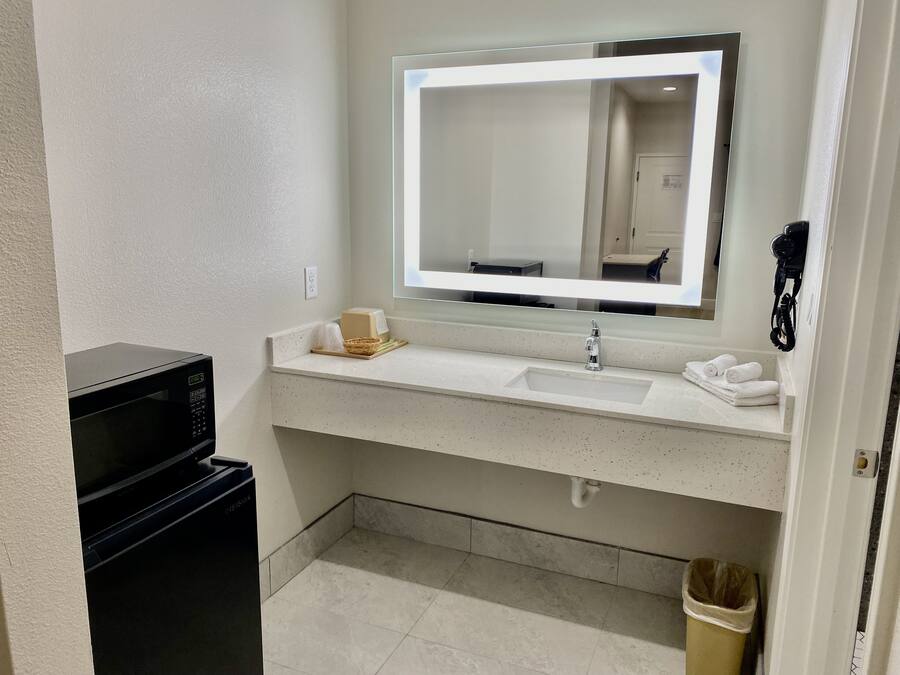 A hotel bathroom with a white sink, a mirror with lights, a black telephone, and a trash can.