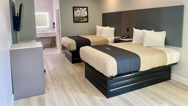 A modern hotel room with a large bed, a desk, and a bathroom visible in the background. - Bluestar Inn (Houston)