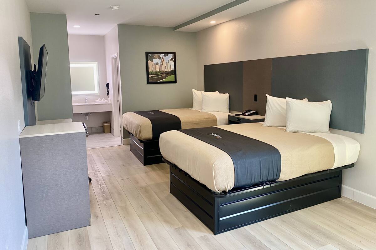 A modern hotel room with a large bed, a desk, and a bathroom visible in the background.