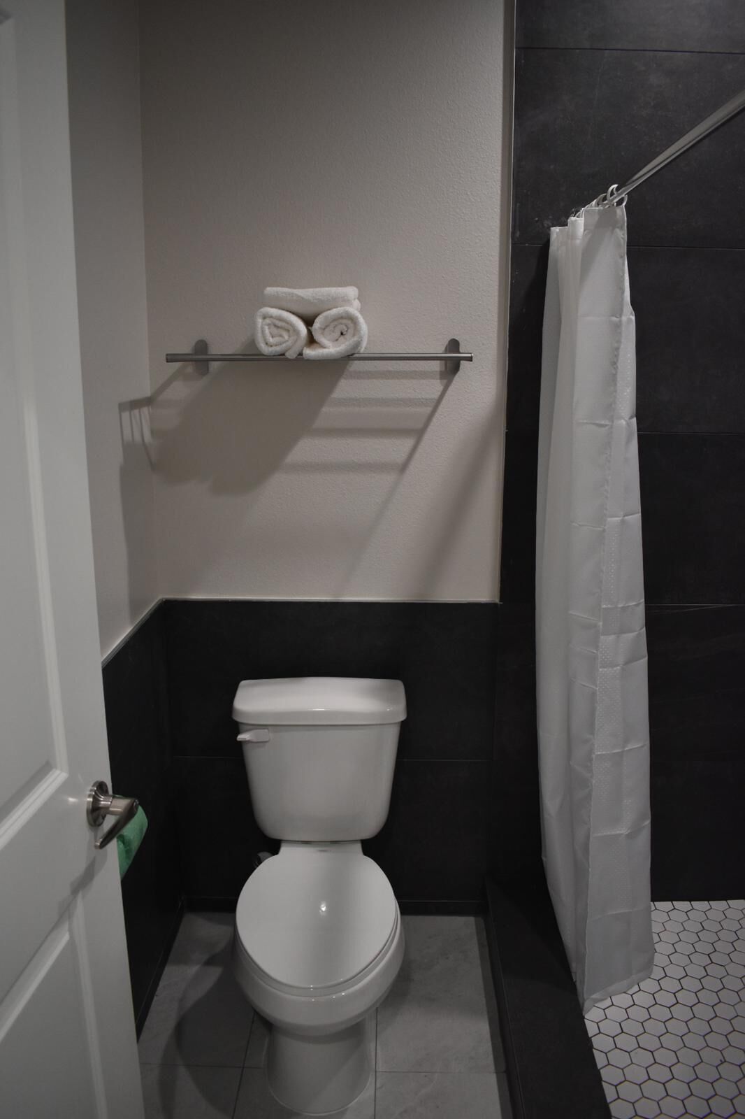A bathroom with a toilet, a towel rack with rolled towels, and a shower curtain.