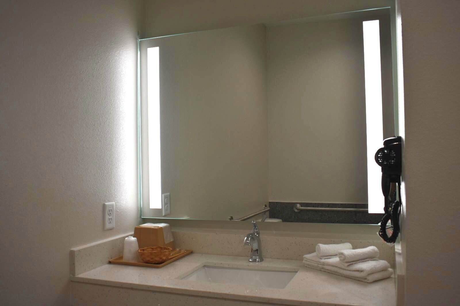 Un baño con lavamanos, espejo y secador de pelo en la pared.
