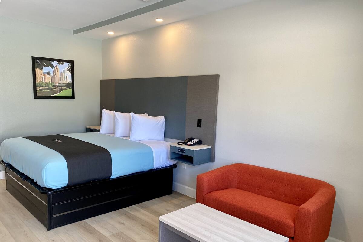 A modern hotel room with a bed, bedside table, and a red armchair.