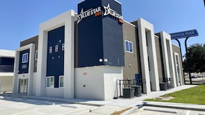 A modern hotel with a prominent Blue Star Inn sign, a parking lot, and a nearby bank. - Bluestar Inn (Houston)