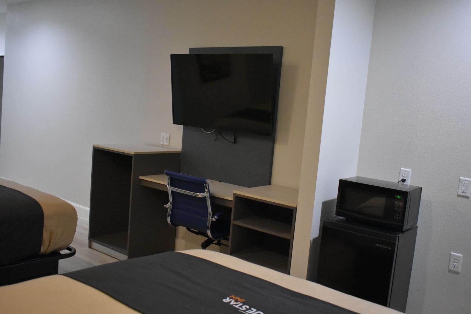 Habitación de hotel con cama, escritorio con silla, televisor montado en la pared y microondas sobre una mesita.