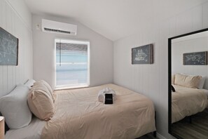 A bedroom with a bed, a bedside table, a mirror, and a window with blinds.