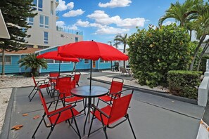 An outdoor patio with red chairs and a table, a red umbrella, and a blue building in the background.
