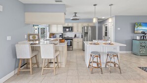 Une cuisine moderne avec des meubles blancs, un îlot central, des tabourets de bar et un ventilateur de plafond.