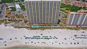 A high-rise hotel with multiple balconies, a pool, and a beach area with umbrellas and sun loungers.