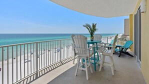 A balcony with a view of the beach and ocean. There are white chairs and a table with a plant.