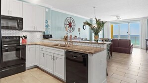 A modern kitchen with white cabinets, a granite countertop, a built-in dishwasher, and a large island with a sink.