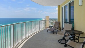 Un balcon avec vue sur l’océan, deux chaises, une petite table et une fenêtre.